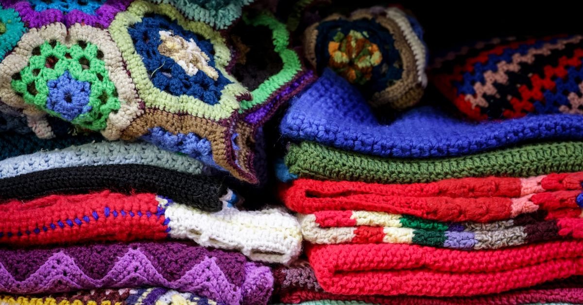 Cobertores de crochê coloridos empilhados, em referência a doações para pessoas em situação de rua