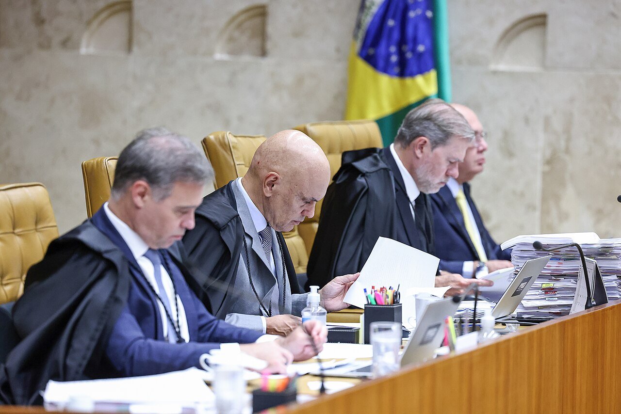 Ministros do Supremo Tribunal Federal durante sessão plenária, com a bandeira do Brasil ao fundo