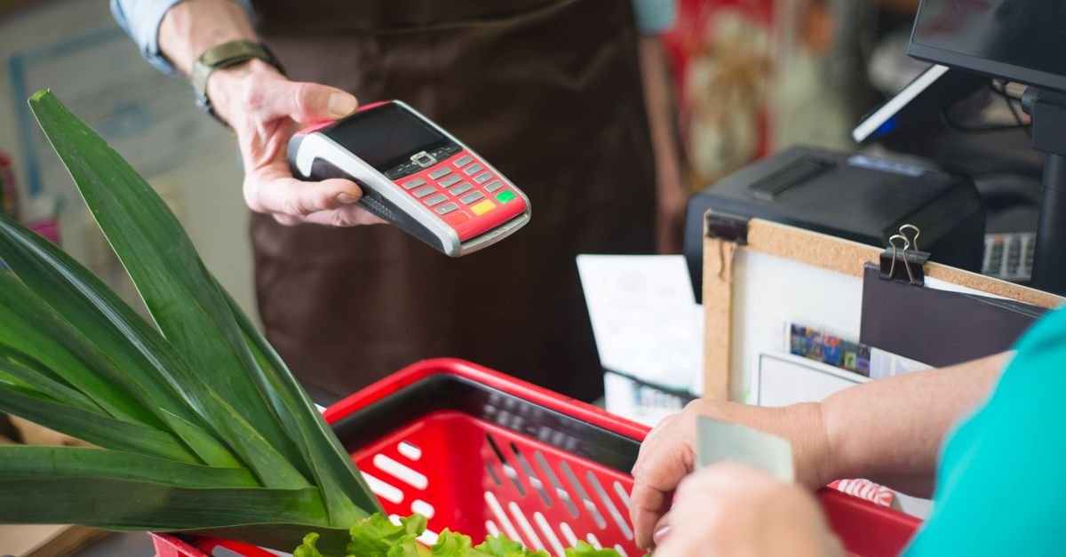 Operador de caixa aproxima maquininha de cartão para pagamento de cliente em supermercado