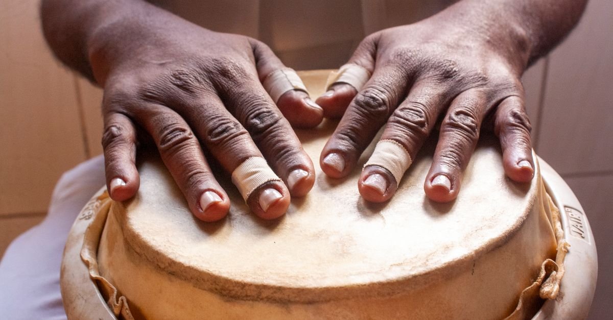 Mãos de percussionista sobre o couro de um tambor artesanal em close