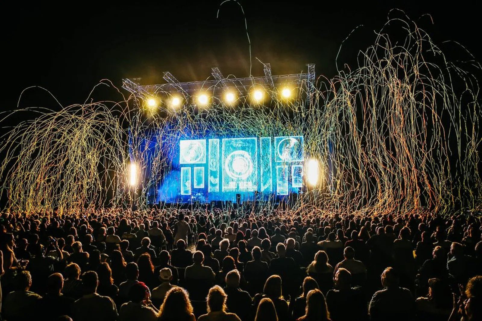 Público em festival ao ar livre diante de palco iluminado