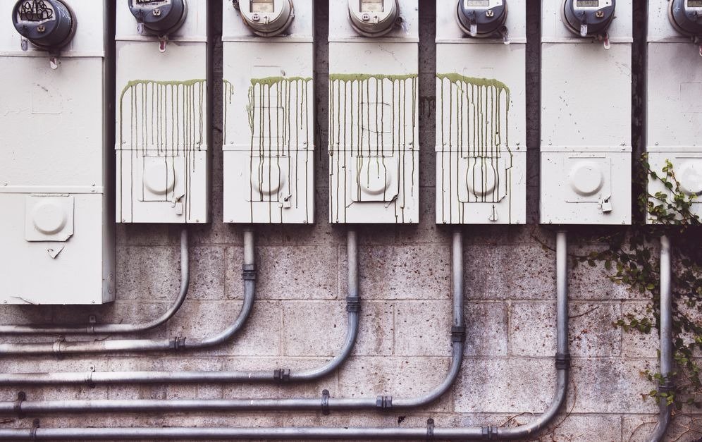 Fileira de medidores de energia elétrica instalados na parede externa de um edifício, com tubulações aparentes
