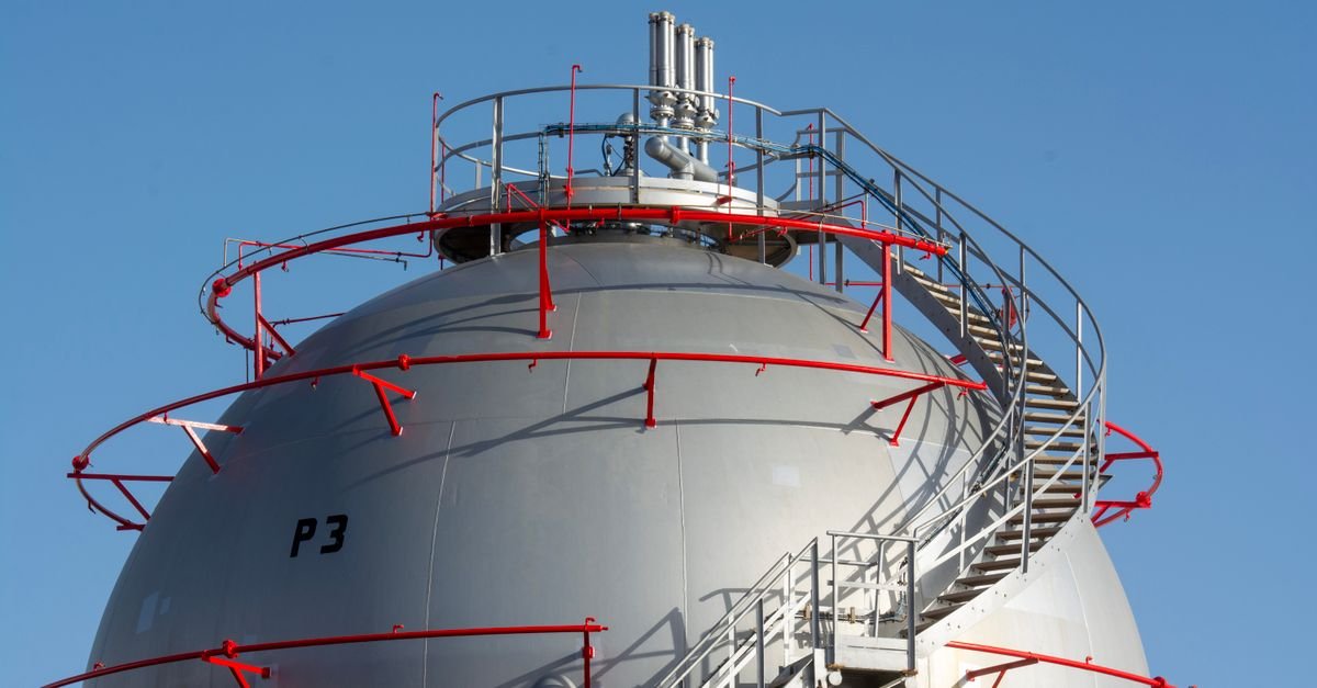Esfera industrial de armazenamento de gás com escada metálica e céu azul ao fundo