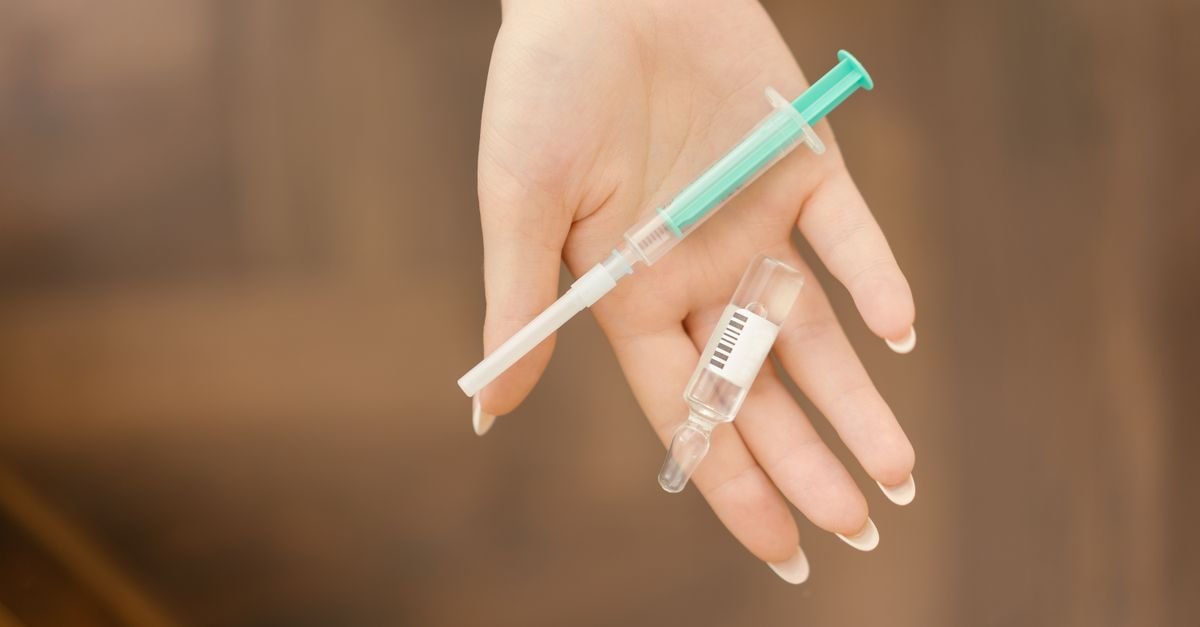 Mão segurando uma seringa e uma ampola de medicamento injetável