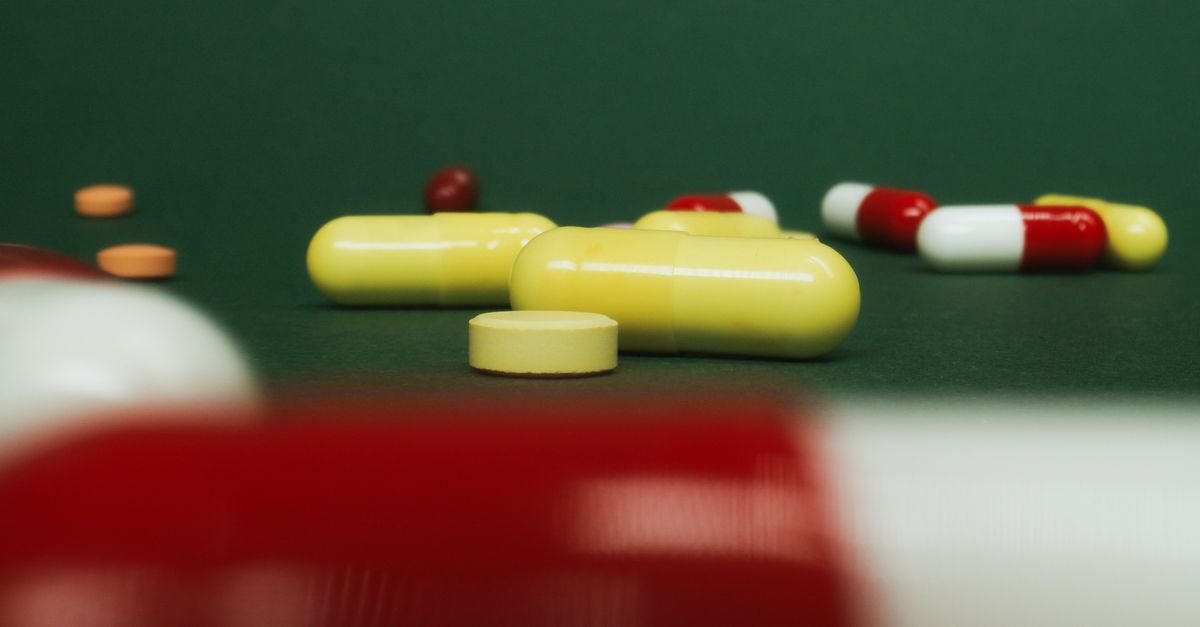 Cápsulas e comprimidos de medicamentos espalhados sobre superfície verde, em close