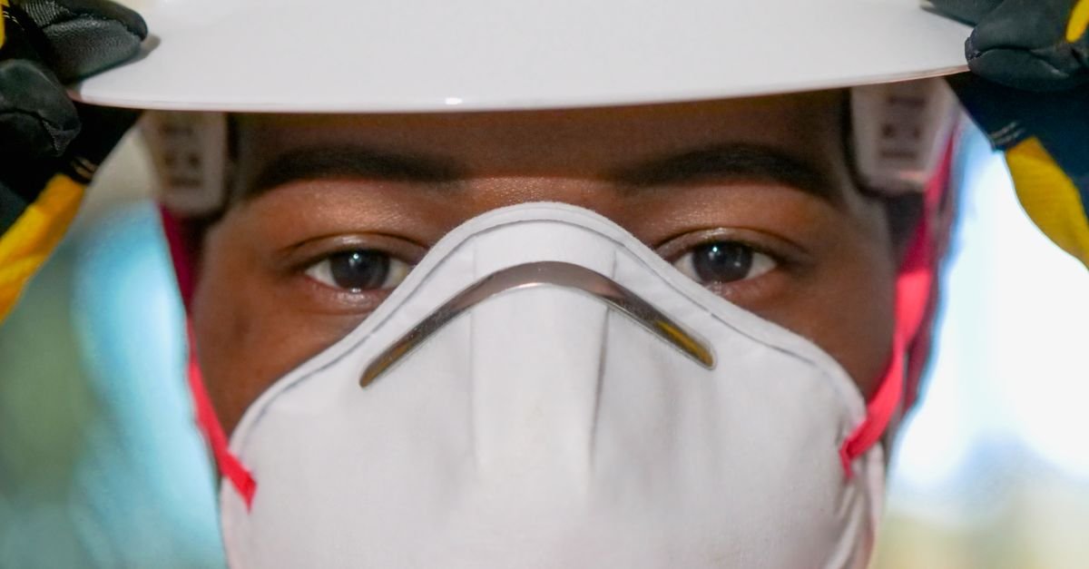 Trabalhador de capacete branco e máscara de proteção respiratória em close
