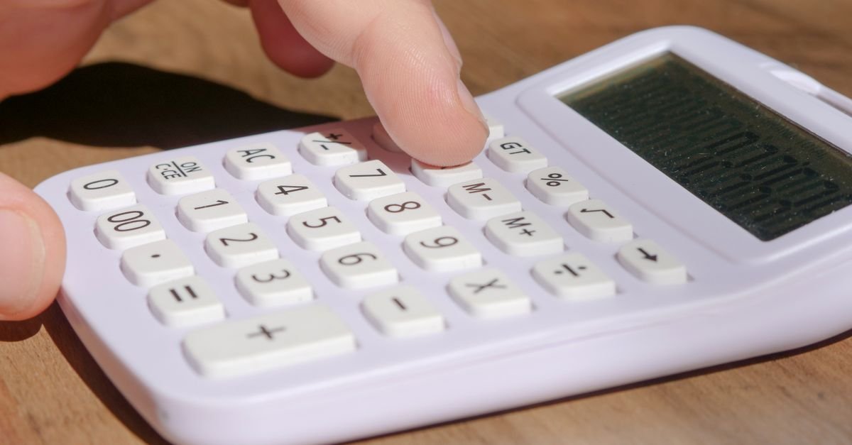 Dedo pressionando as teclas de uma calculadora branca sobre mesa de madeira