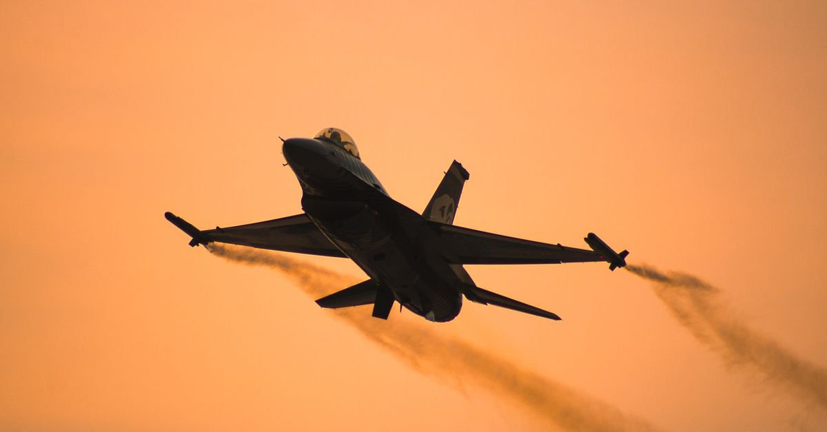 Silhueta de caça F-16 em voo contra céu alaranjado ao entardecer