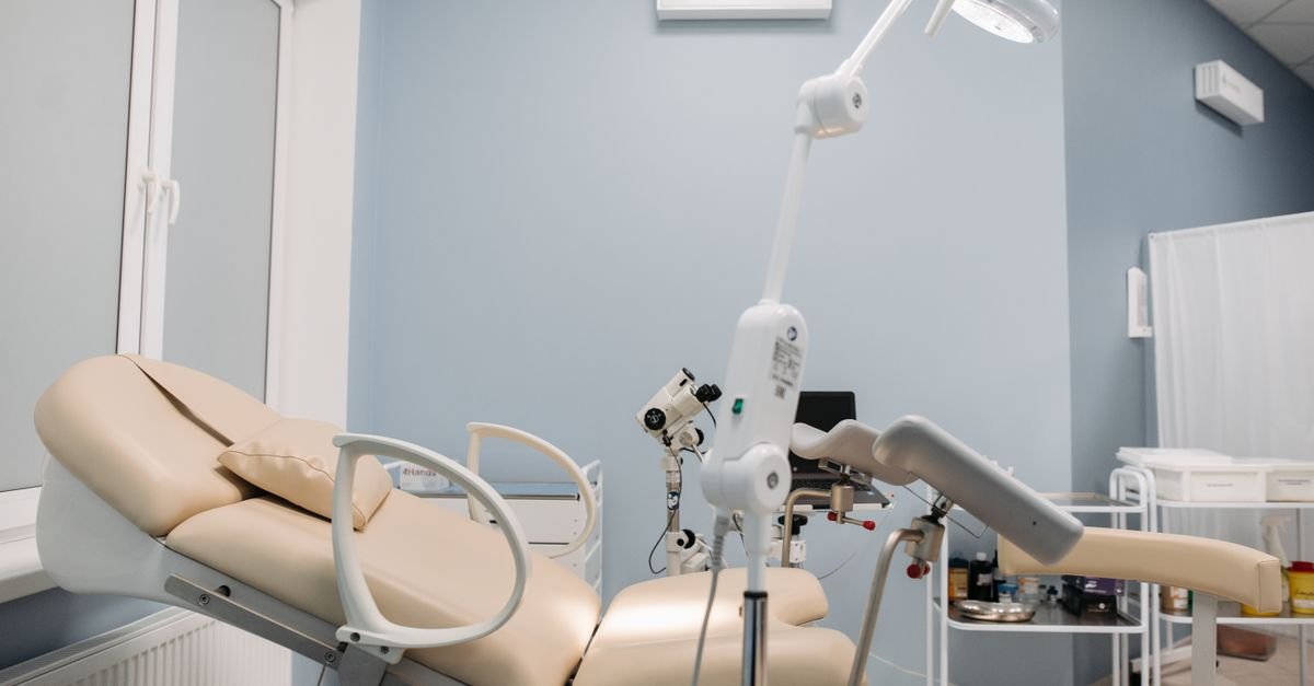 Consultório ginecológico vazio, com maca de exame e equipamento clínico