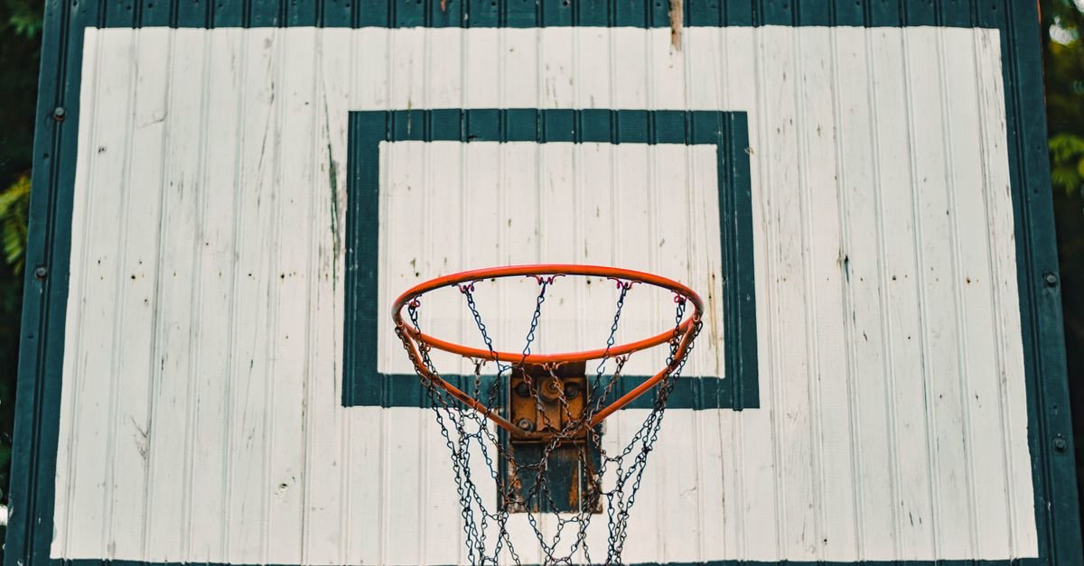 Cesta de basquete com aro laranja e rede de corrente presa a uma tabela de madeira