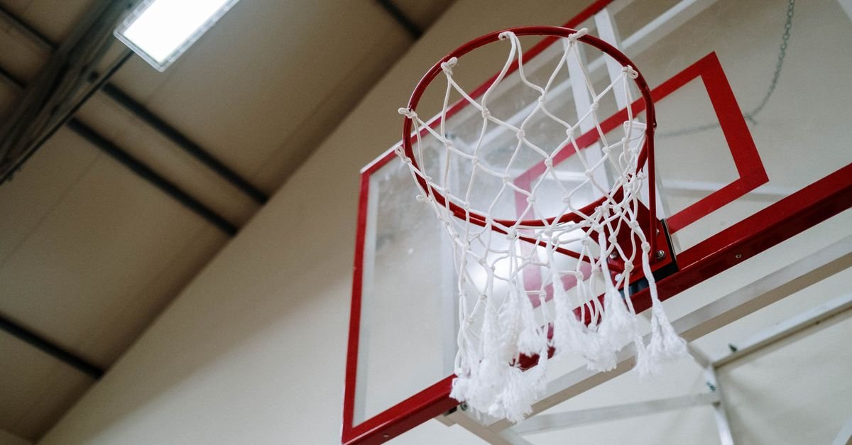 Aro de basquete com rede branca visto de baixo em ginásio coberto