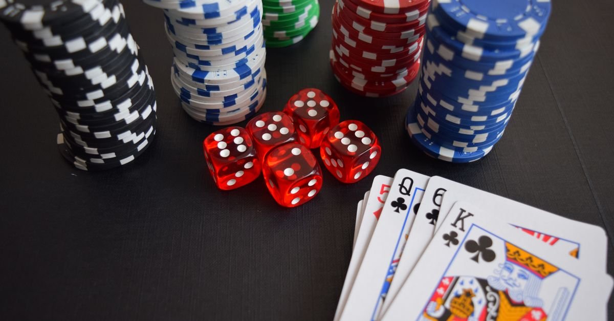 Fichas de pôquer, dados vermelhos e cartas de baralho sobre mesa escura