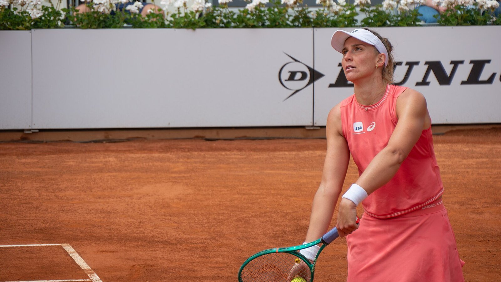 A tenista Beatriz Haddad Maia, de uniforme rosa e viseira branca, aguarda o saque em quadra de saibro