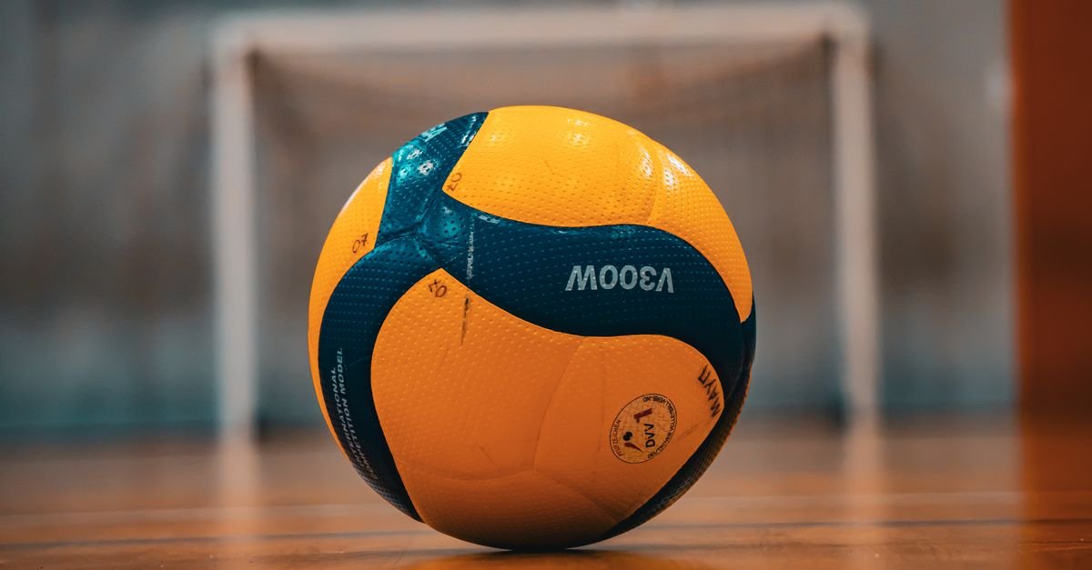 Bola oficial de vôlei amarela e azul sobre quadra indoor
