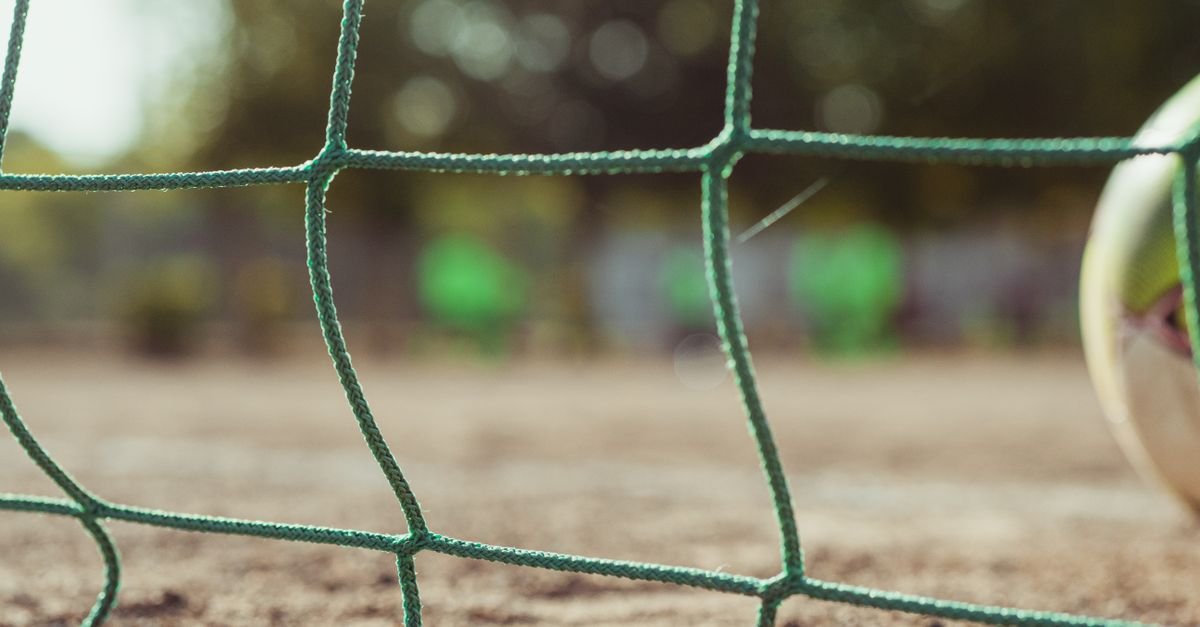 Rede de gol de futebol em primeiro plano com bola ao lado do campo