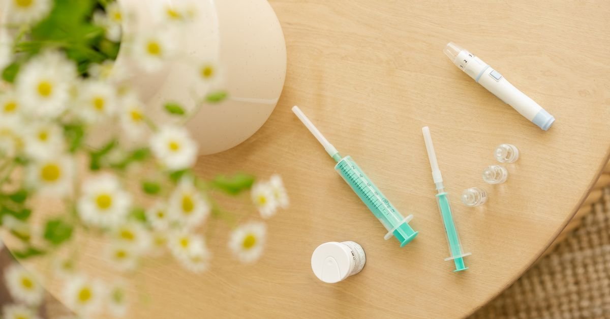 Caneta injetora, seringas e frasco de medicamento sobre mesa de madeira
