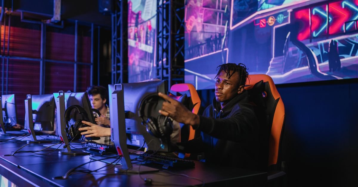 Jovens jogam em computadores enfileirados em arena de esports com iluminação colorida