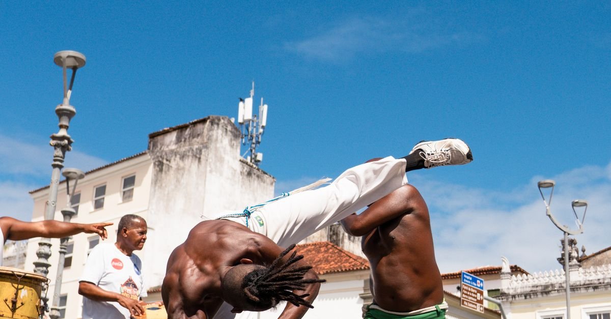Roda de capoeira em rua do centro histórico de Salvador, com capoeiristas de calça branca e atabaque