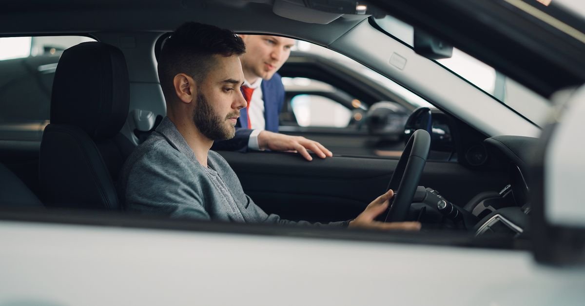Cliente sentado ao volante de um carro em concessionária ao lado de vendedor