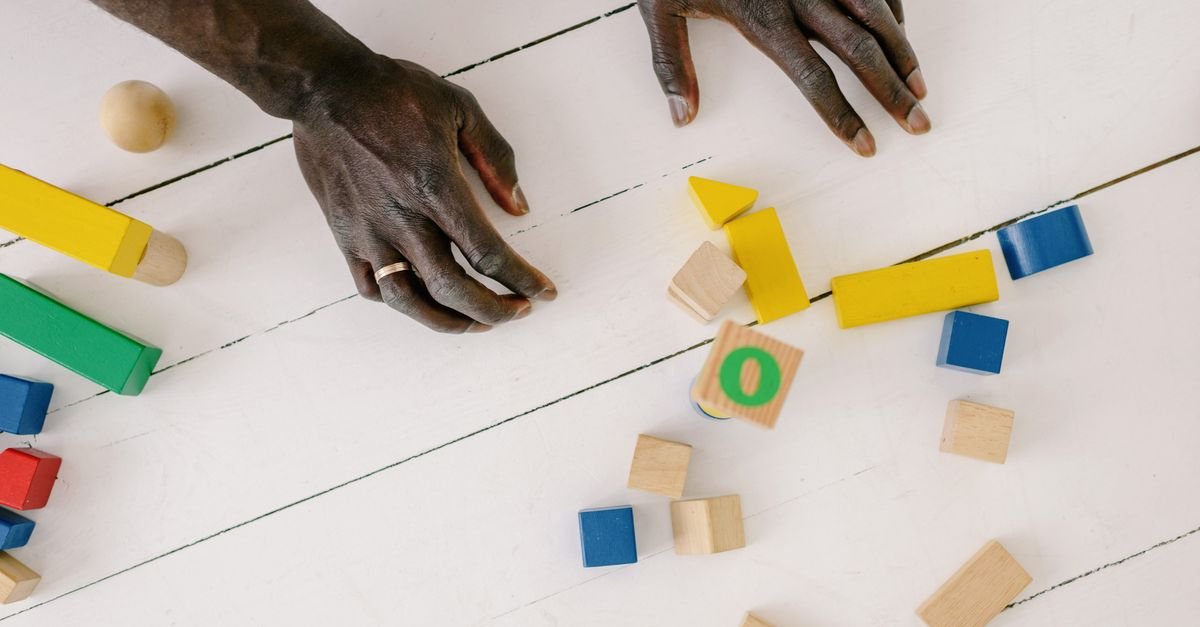 Mãos de adulto brincando com blocos coloridos de madeira sobre mesa branca