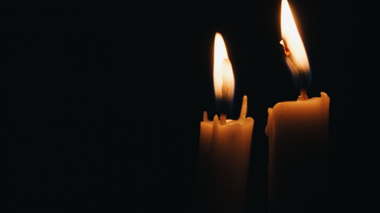 Duas velas acesas em fundo escuro, em símbolo de luto