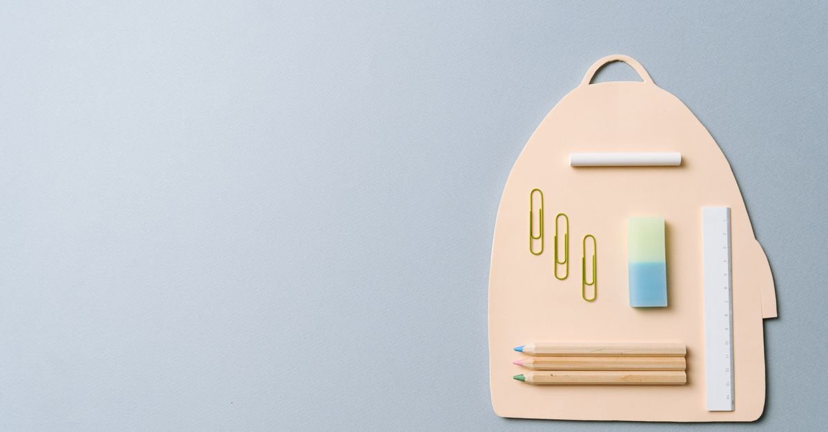 Material escolar disposto sobre fundo cinza formando o desenho de uma mochila