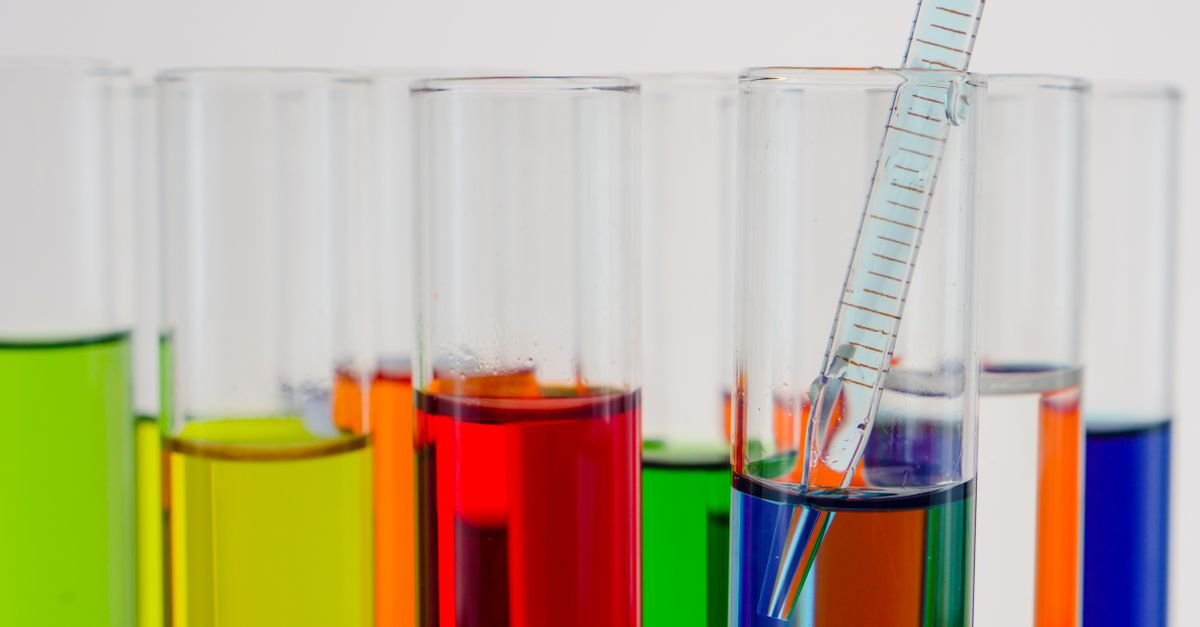Tubos de ensaio com líquidos coloridos e pipeta de vidro em bancada de laboratório