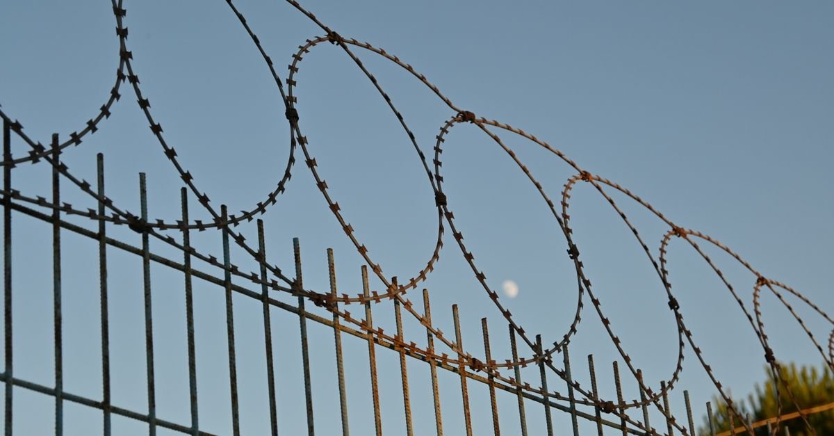 Cerca metálica encimada por rolos de arame farpado recortada contra o céu