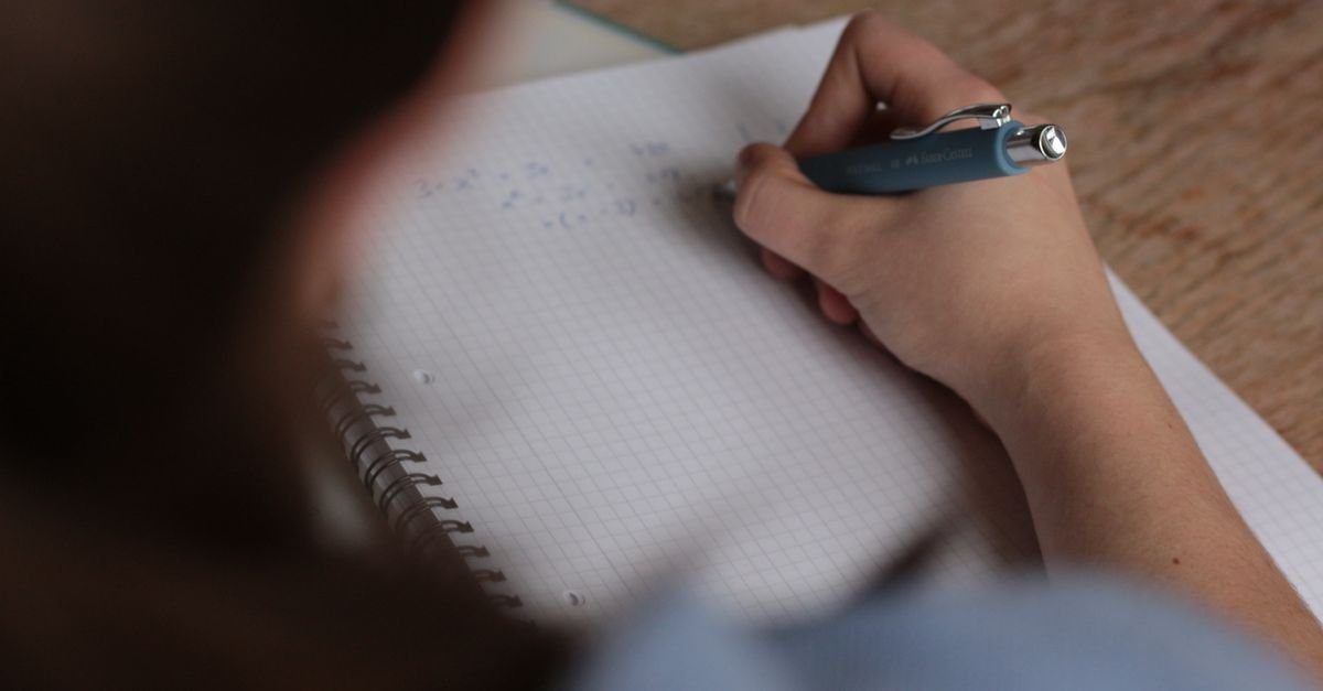 Estudante escreve equações em caderno quadriculado durante preparação para concurso