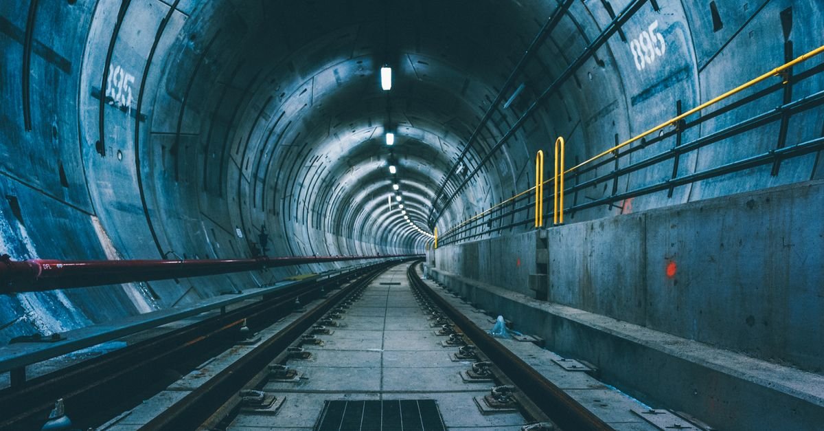 Túnel de metrô moderno com trilhos ao centro e iluminação no teto