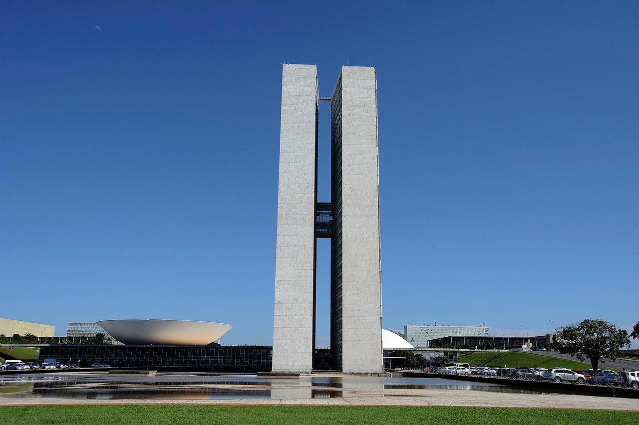 Torres do Congresso Nacional vistas de frente, com o espelho d'água e a cúpula do plenário da Câmara ao fundo