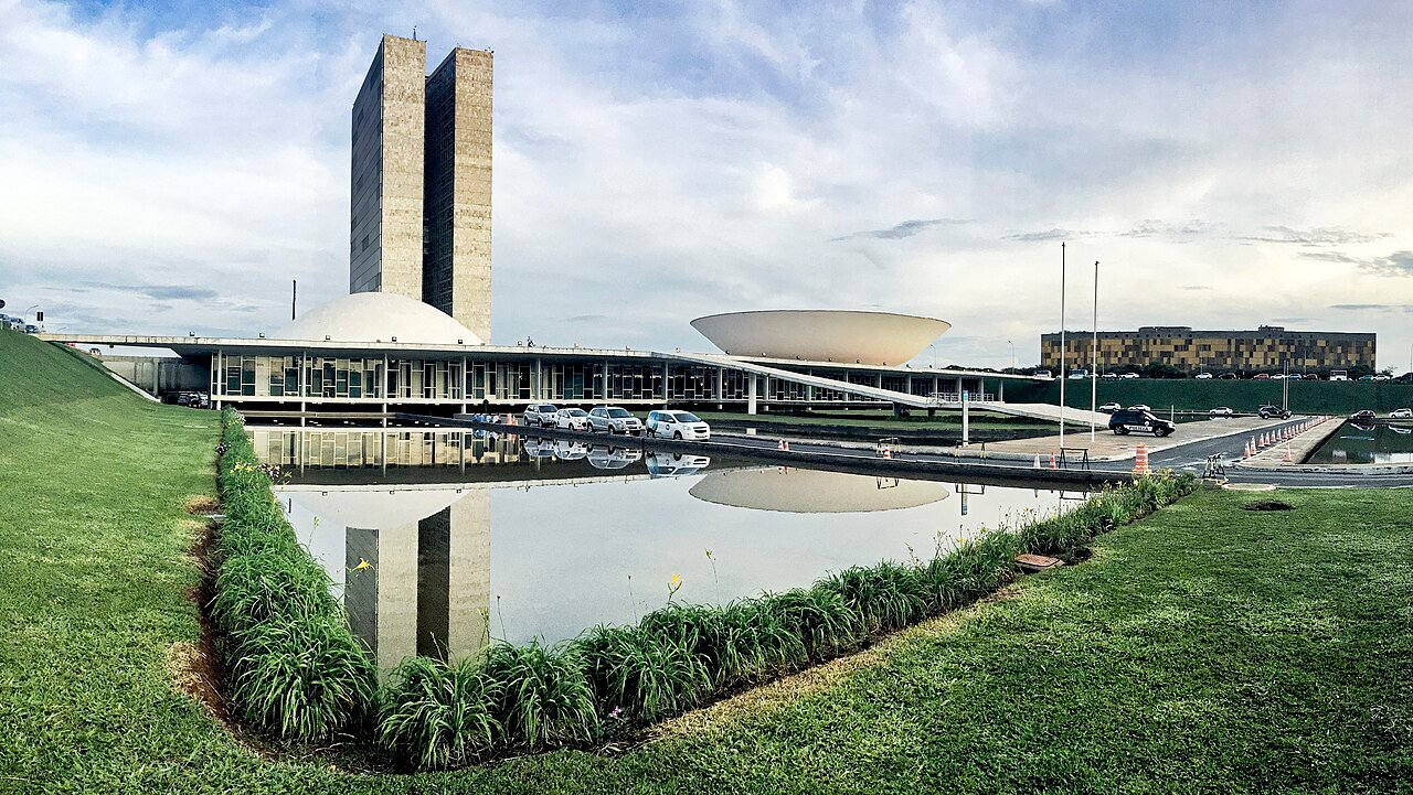 Vista externa do Congresso Nacional, em Brasília, com as torres e as cúpulas refletidas no espelho d água