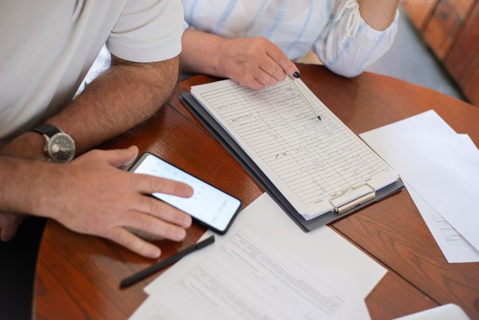 Casal confere contas e documentos com prancheta e celular sobre a mesa