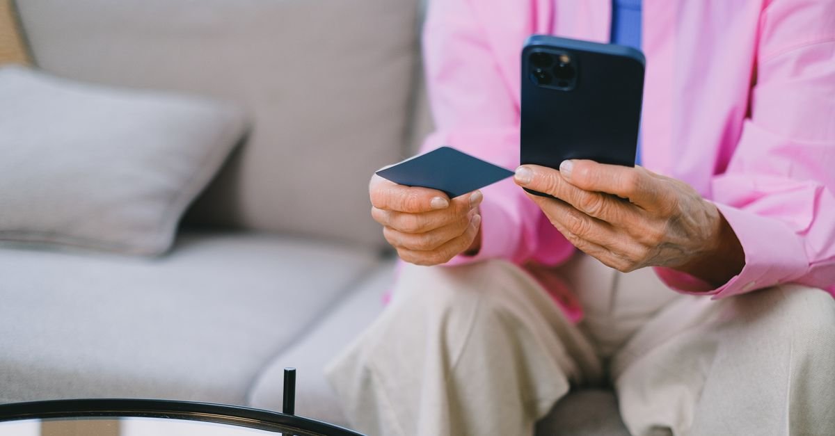 Idoso segura cartão e smartphone para operação financeira
