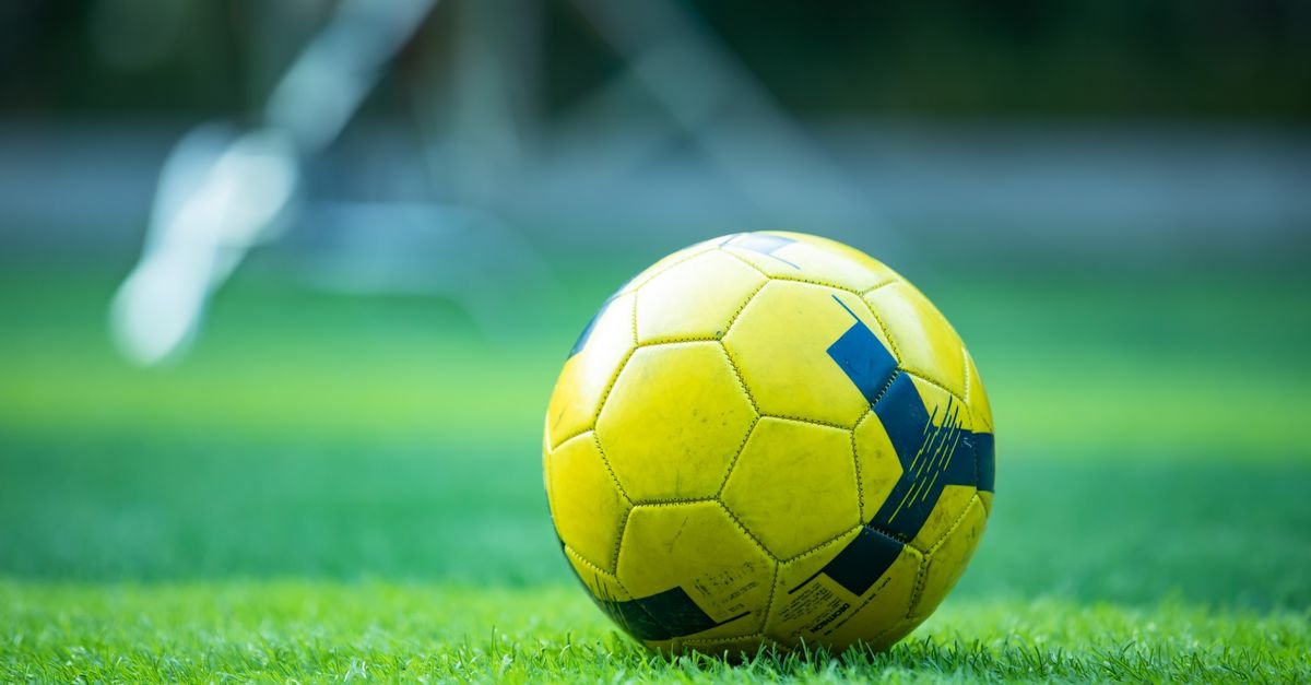 Bola de futebol amarela parada sobre o gramado verde de um campo
