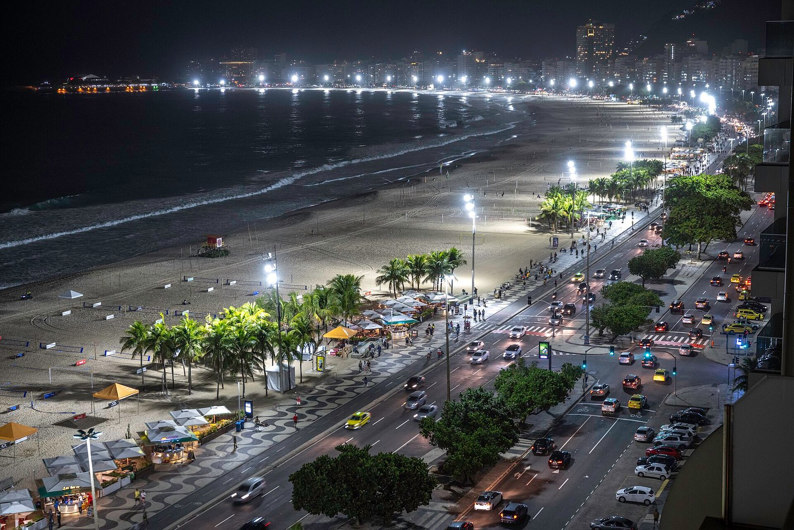 Vista noturna em plano aberto da praia de Copacabana, do calçadão e da Avenida Atlântica, no Rio de Janeiro