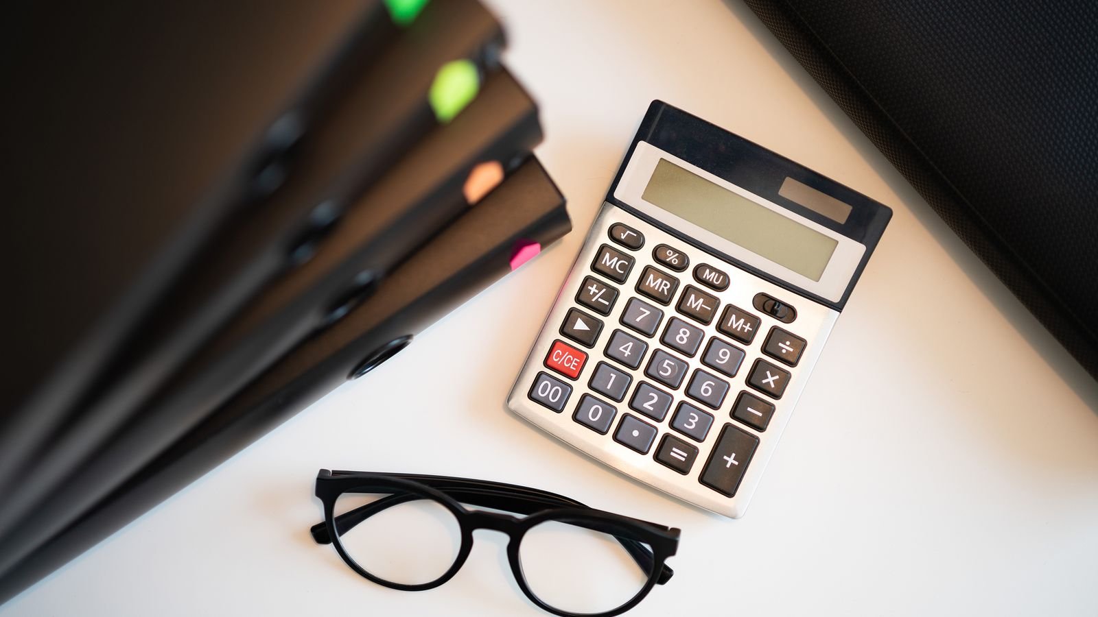 Calculadora sobre mesa de escritório com pastas e óculos