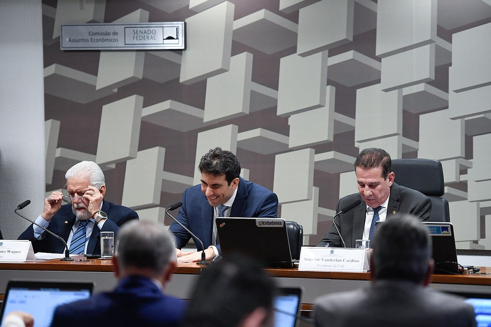 Gabriel Galípolo sentado à mesa da Comissão de Assuntos Econômicos do Senado, entre dois senadores, durante sabatina