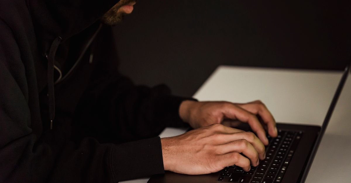Homem de moletom com capuz digitando em teclado de notebook em ambiente escuro