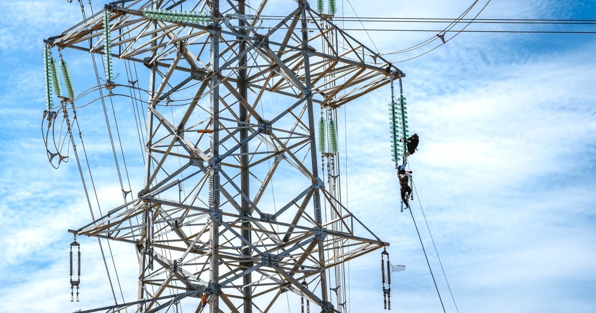 Equipe faz manutenção em torre de energia elétrica sob céu azul