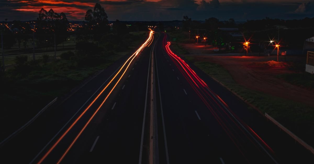 Rodovia de duas pistas à noite com rastros de luz de veículos