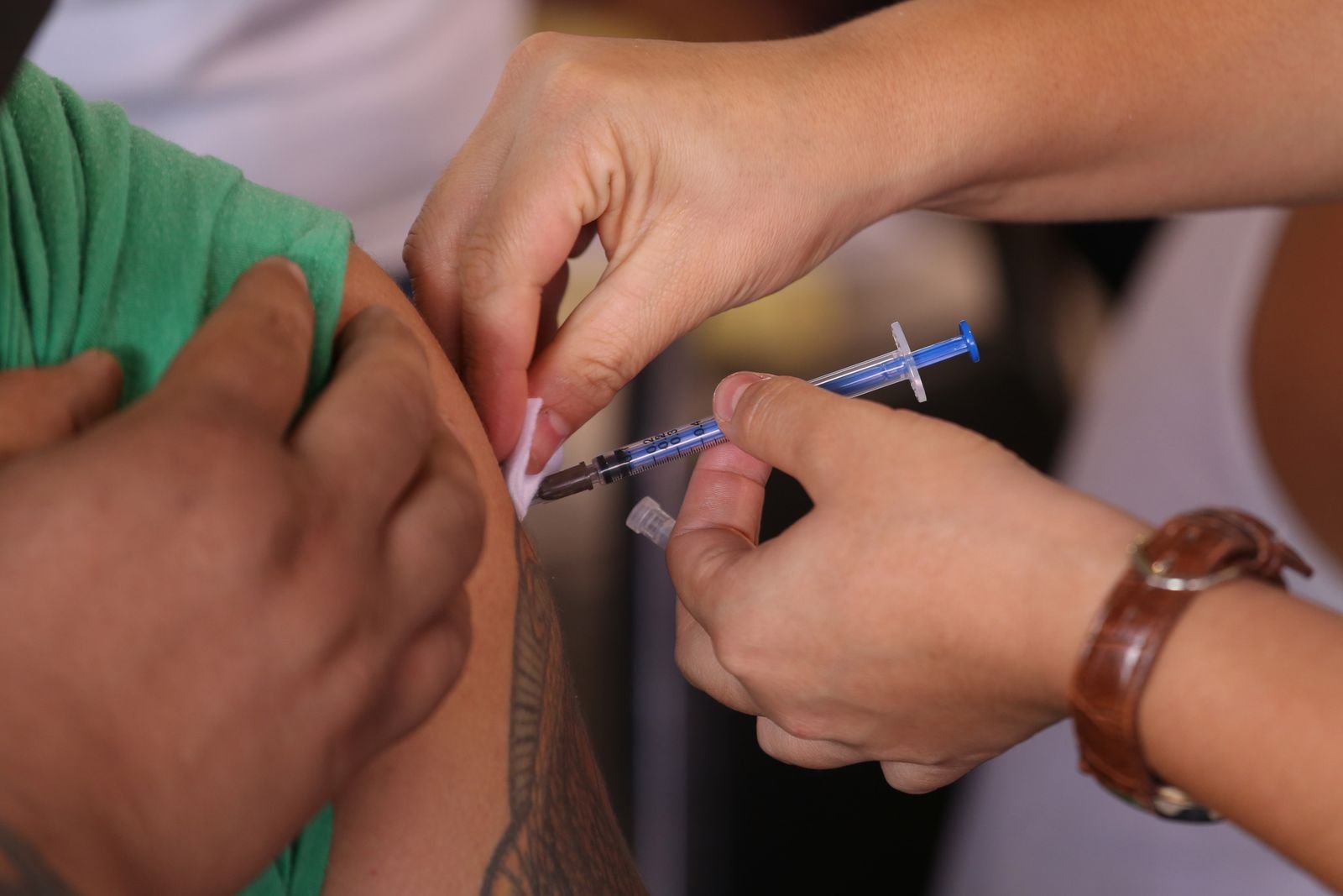 Profissional de saude aplica vacina no braco de paciente em sala de vacinacao