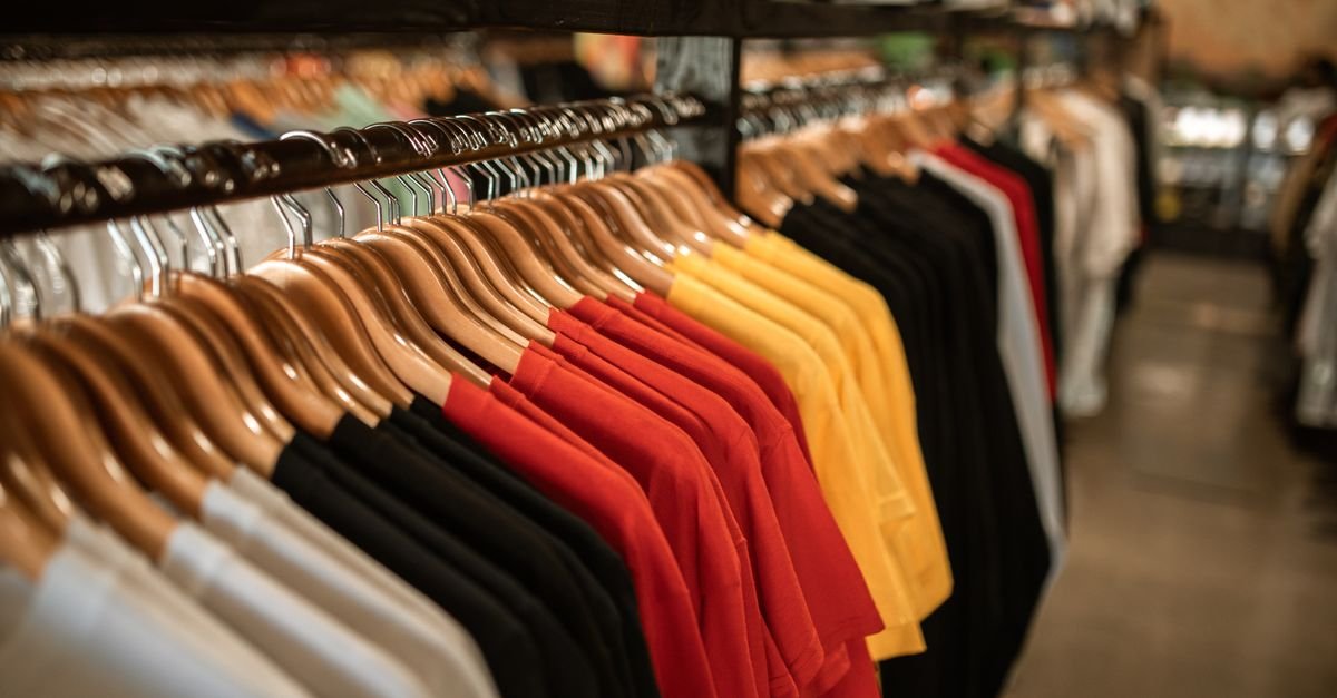 Araras de loja de roupas com camisetas coloridas penduradas em cabides de madeira
