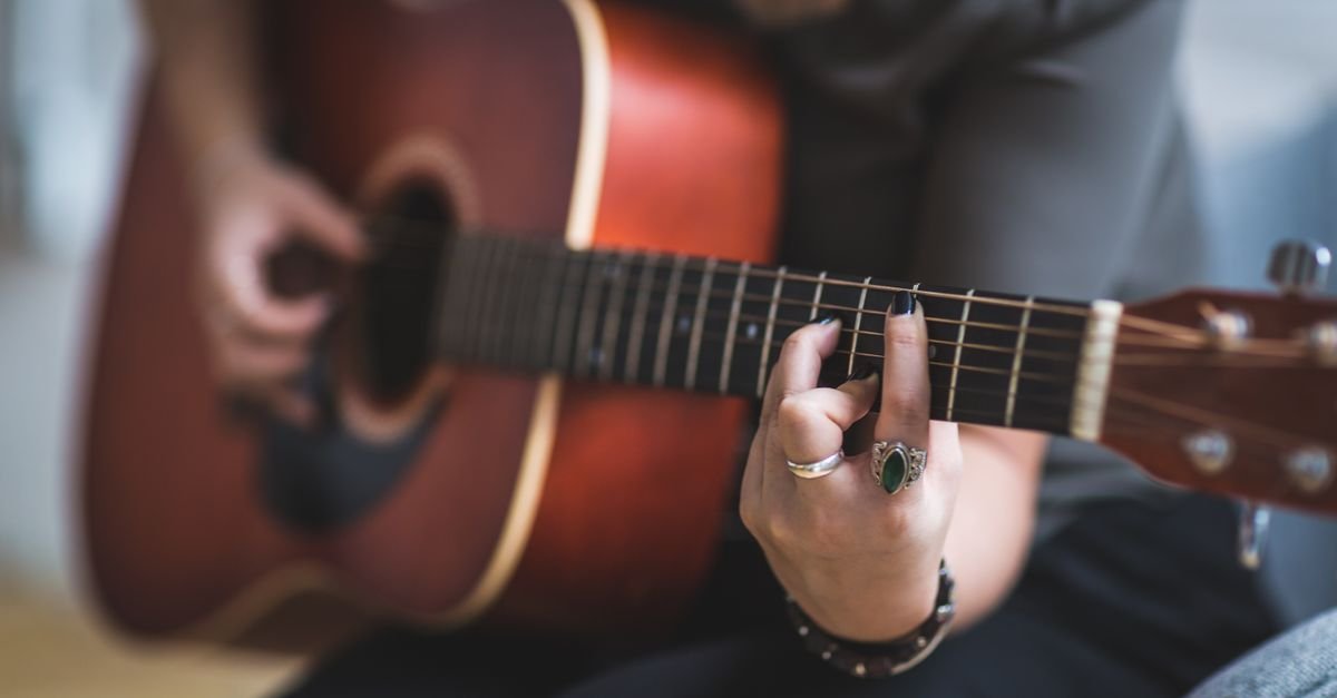 Mãos de uma mulher tocando um violão de cordas de aço em primeiro plano