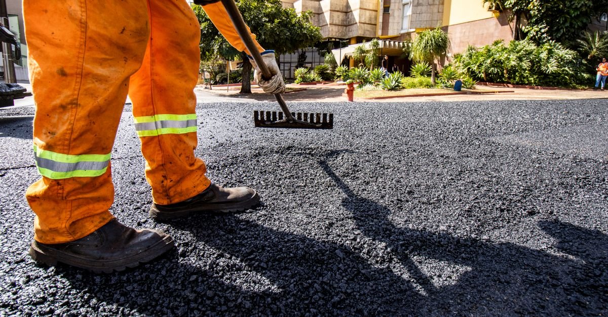 Operário nivela asfalto novo em via urbana durante obra de pavimentação