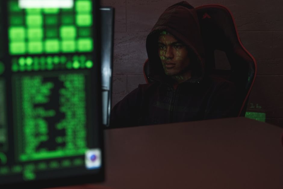 Hacker encapuzado diante de tela com codigo, simbolizando ataque ao sistema de alertas
