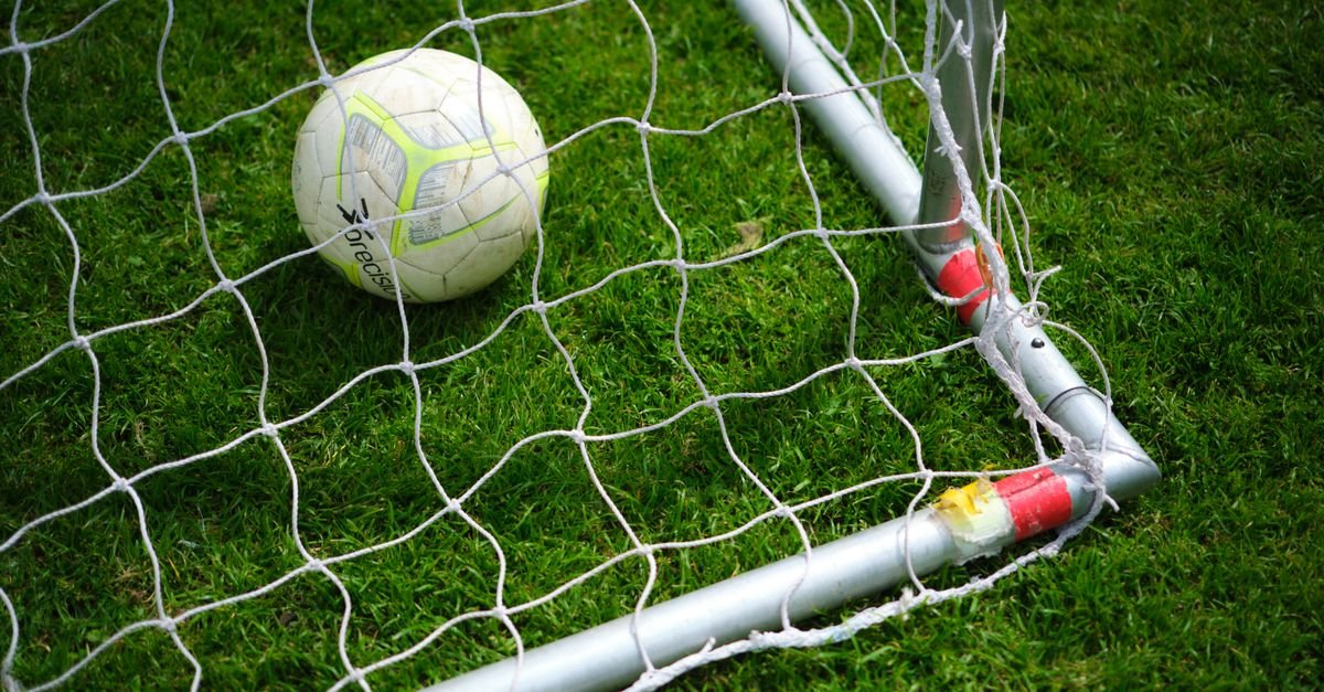 Close-up image of a soccer ball resting in a goal net on a vibrant green grass field.
