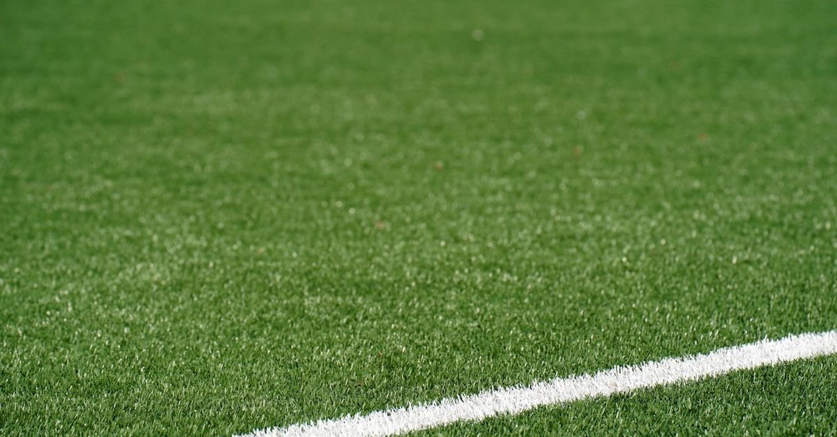 Close-up view of a green artificial soccer field with a white boundary line and space for text.