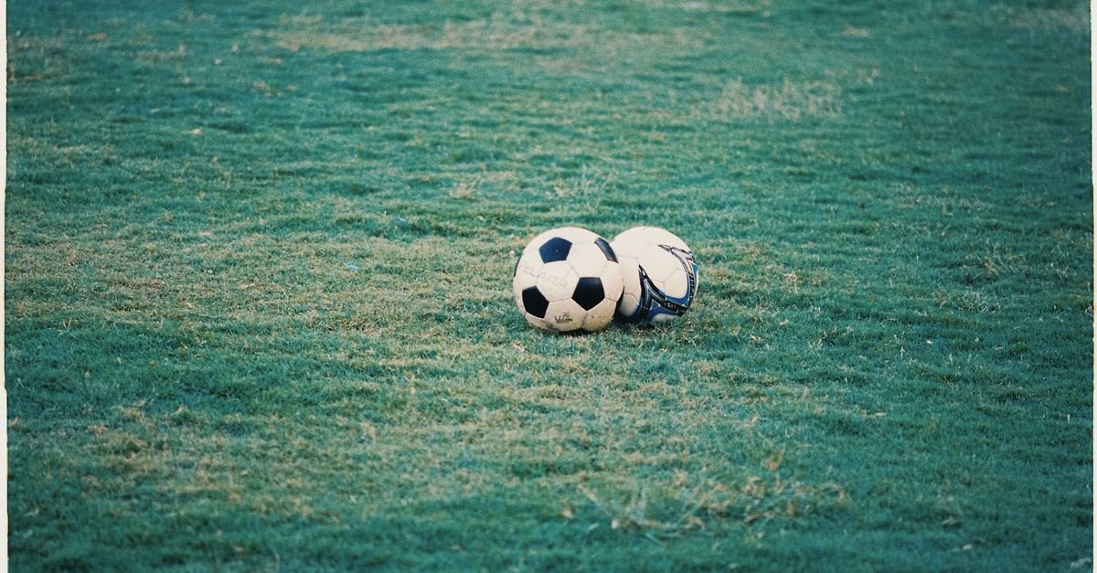 Two soccer balls resting on a lush green field, perfect for sports themes.