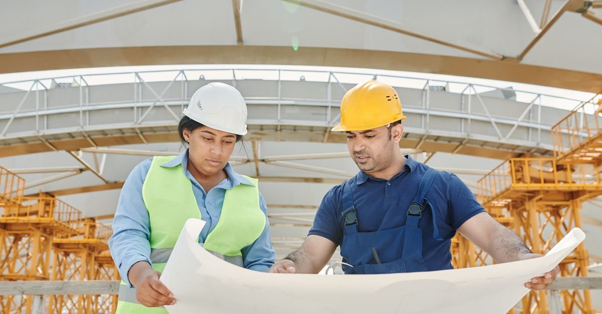 Male and female engineers discussing blueprints at a construction site, promoting teamwork and planning.